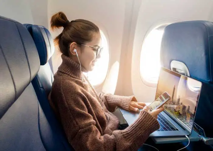 Persona en un avión con laptop y teléfono celular